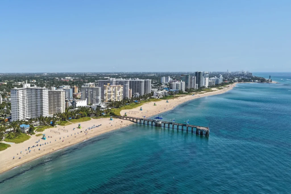 Aerial view of Pompano Beach, Florida, with the beachfront, the Fisher Family Pier and the Hillsboro Inlet Lighthouse in the distance